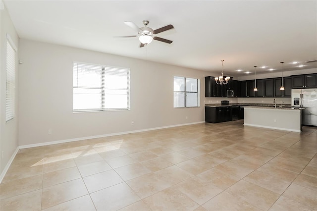 unfurnished living room with light tile patterned floors, baseboards, and ceiling fan with notable chandelier