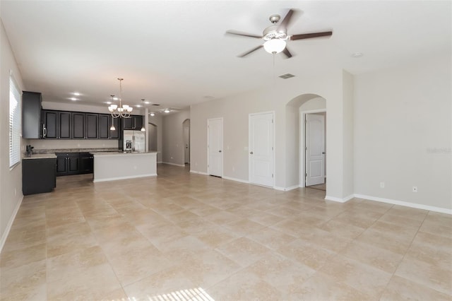 unfurnished living room featuring arched walkways, ceiling fan with notable chandelier, visible vents, and baseboards