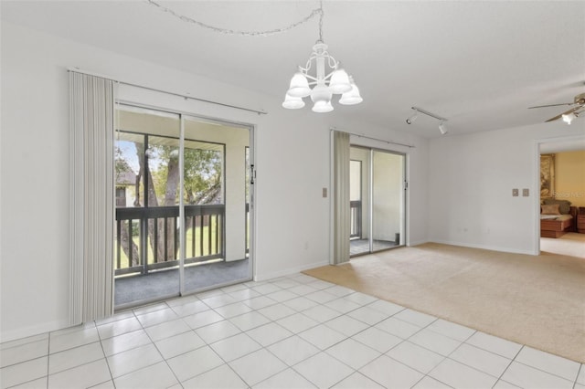 unfurnished room featuring ceiling fan with notable chandelier, rail lighting, light tile patterned floors, baseboards, and light colored carpet