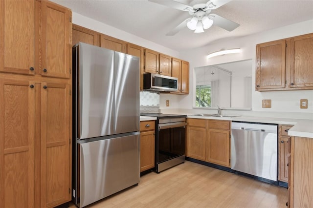 kitchen with brown cabinetry, a sink, stainless steel appliances, light countertops, and light wood-style floors