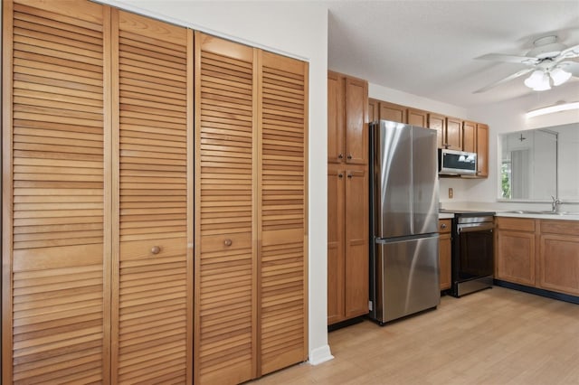 kitchen with light countertops, appliances with stainless steel finishes, light wood-style floors, brown cabinetry, and a sink