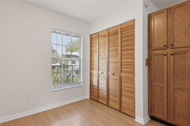 unfurnished bedroom with a closet, multiple windows, baseboards, and light wood-style flooring