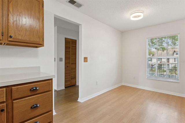 unfurnished room featuring visible vents, baseboards, light wood-style floors, and a textured ceiling