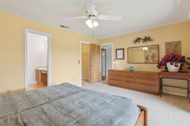 bedroom featuring visible vents, a walk in closet, light colored carpet, ensuite bath, and a ceiling fan