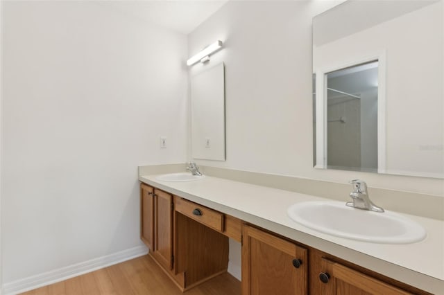 full bath with double vanity, wood finished floors, baseboards, and a sink