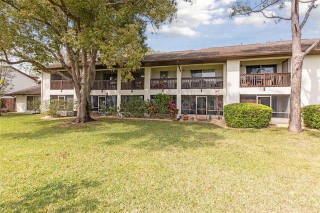 rear view of property with a balcony, stucco siding, and a yard