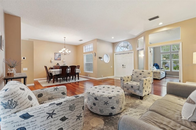 living room featuring visible vents, a notable chandelier, baseboards, and wood finished floors