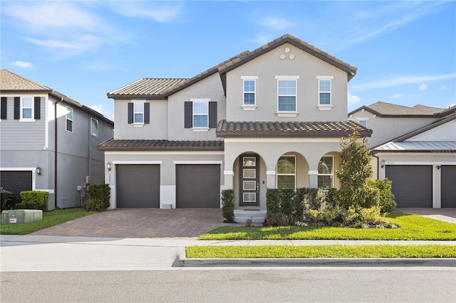 view of front facade featuring decorative driveway, a tile roof, an attached garage, and stucco siding