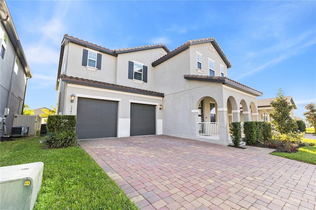 mediterranean / spanish-style home with an attached garage, a gate, decorative driveway, central air condition unit, and stucco siding