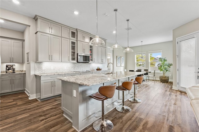 kitchen featuring dark wood-style floors, a breakfast bar area, stainless steel microwave, decorative backsplash, and gray cabinetry