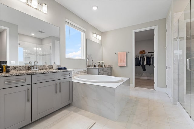 full bathroom featuring a stall shower, visible vents, a garden tub, a walk in closet, and two vanities