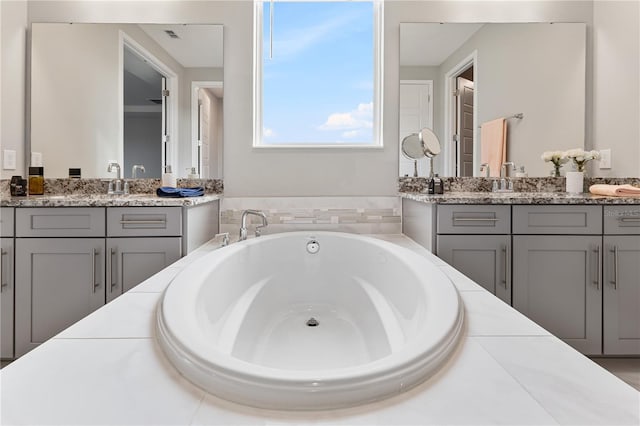 full bath featuring a sink, two vanities, a garden tub, and visible vents