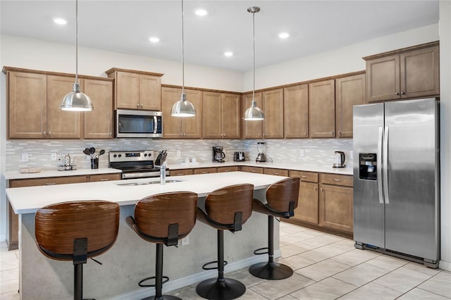 kitchen with a kitchen island with sink, a sink, a kitchen breakfast bar, light countertops, and appliances with stainless steel finishes