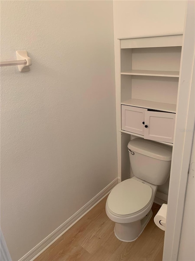 bathroom with toilet, baseboards, and wood finished floors