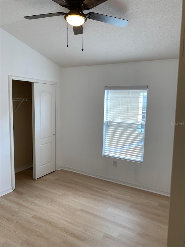 unfurnished bedroom with a textured ceiling, a closet, lofted ceiling, and light wood-style floors