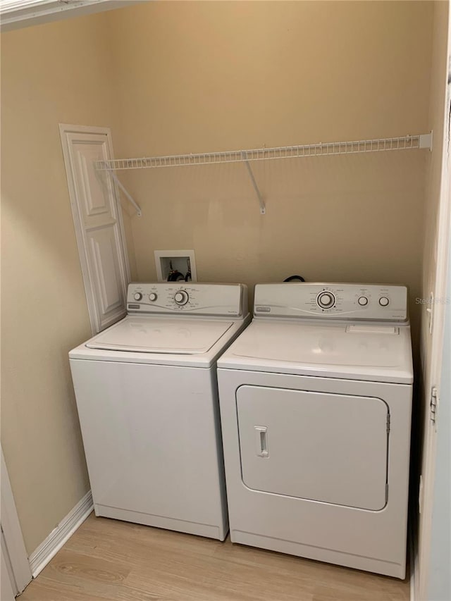 washroom featuring laundry area, baseboards, light wood finished floors, and separate washer and dryer