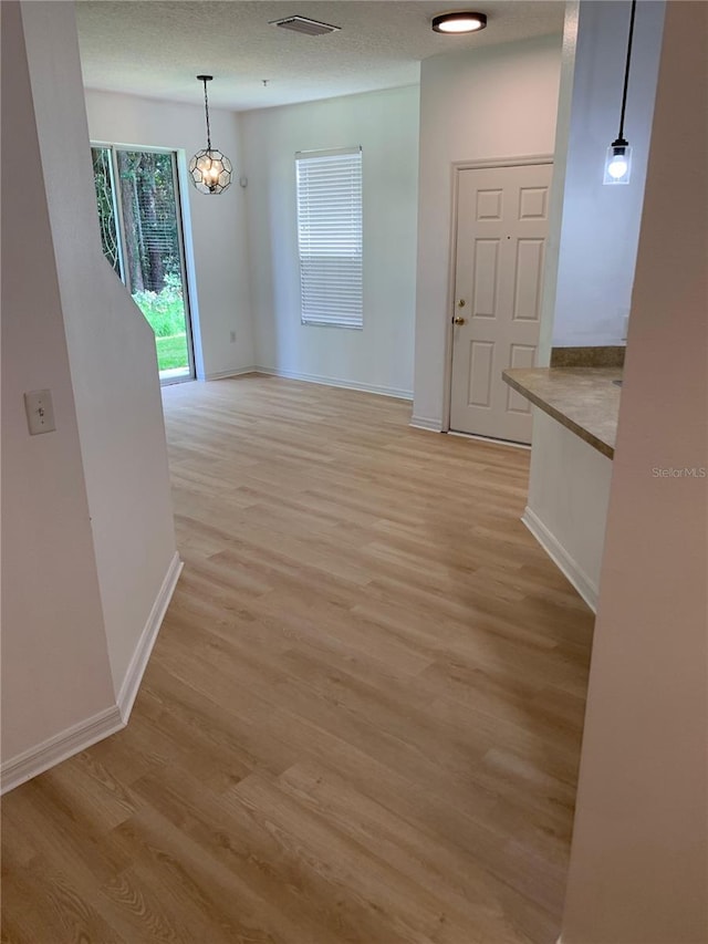 interior space featuring light wood finished floors, visible vents, an inviting chandelier, a textured ceiling, and baseboards