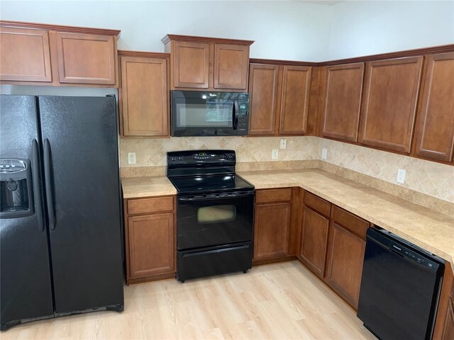 kitchen with light countertops, brown cabinets, black appliances, light wood finished floors, and tasteful backsplash