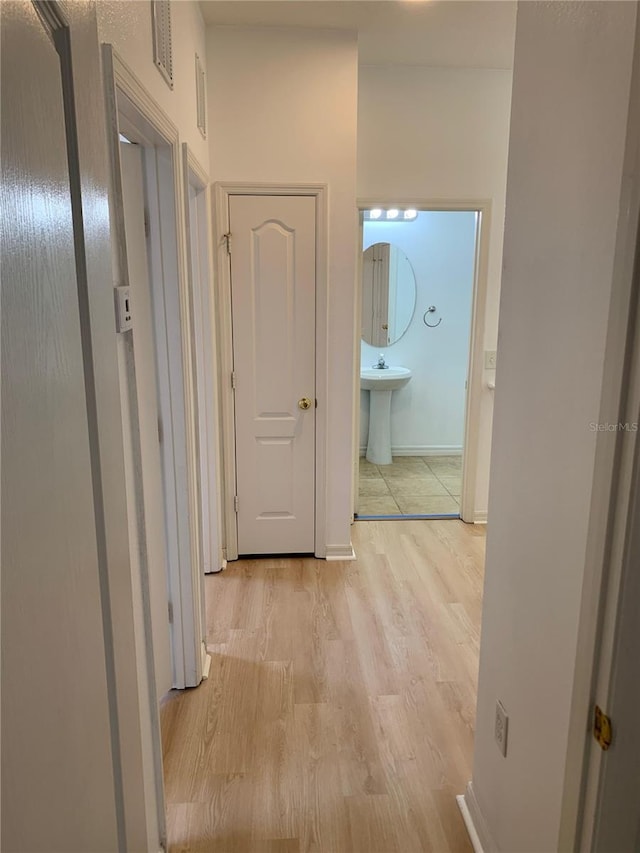 hall featuring light wood finished floors, baseboards, visible vents, and a sink