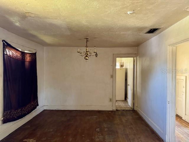 unfurnished dining area with a textured ceiling, a notable chandelier, wood finished floors, visible vents, and baseboards