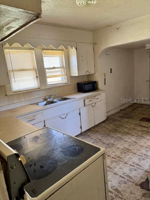 kitchen featuring electric range oven, white cabinetry, a sink, a textured ceiling, and black microwave