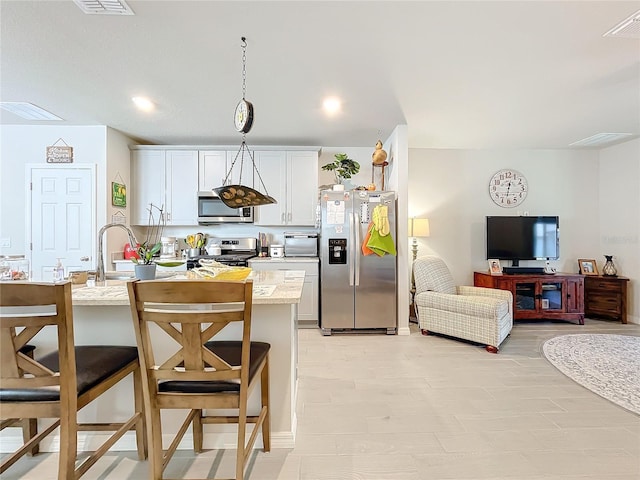 kitchen with appliances with stainless steel finishes, a breakfast bar area, visible vents, and white cabinets