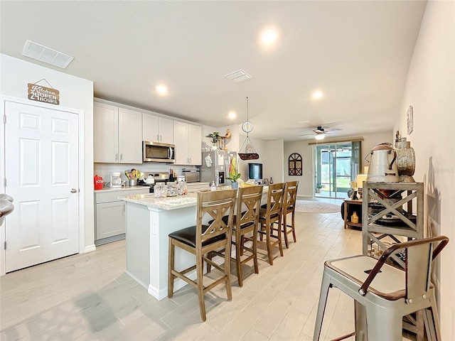 kitchen with visible vents, an island with sink, appliances with stainless steel finishes, a breakfast bar, and light wood-type flooring