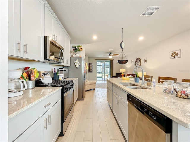 kitchen with stainless steel appliances, visible vents, white cabinetry, a sink, and an island with sink