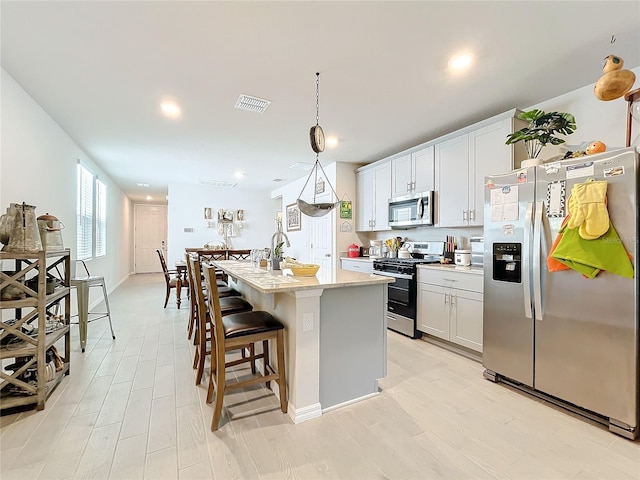 kitchen featuring a center island with sink, stainless steel appliances, visible vents, hanging light fixtures, and a kitchen bar