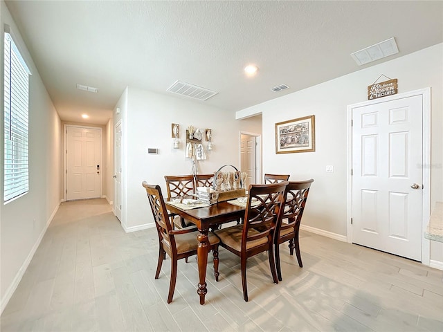 dining room featuring light wood finished floors, baseboards, visible vents, and a textured ceiling