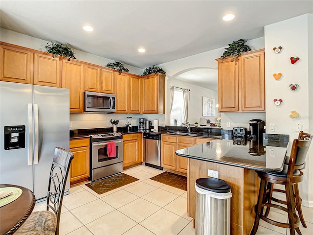 kitchen featuring light tile patterned floors, a peninsula, a sink, a kitchen breakfast bar, and appliances with stainless steel finishes