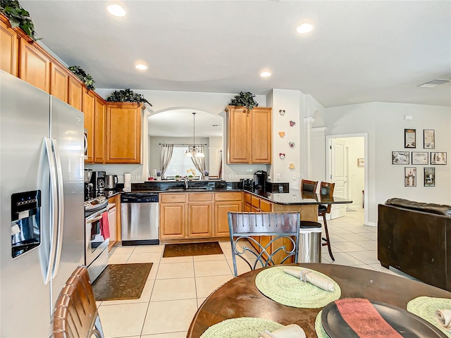 kitchen featuring dark countertops, appliances with stainless steel finishes, a peninsula, a sink, and light tile patterned flooring