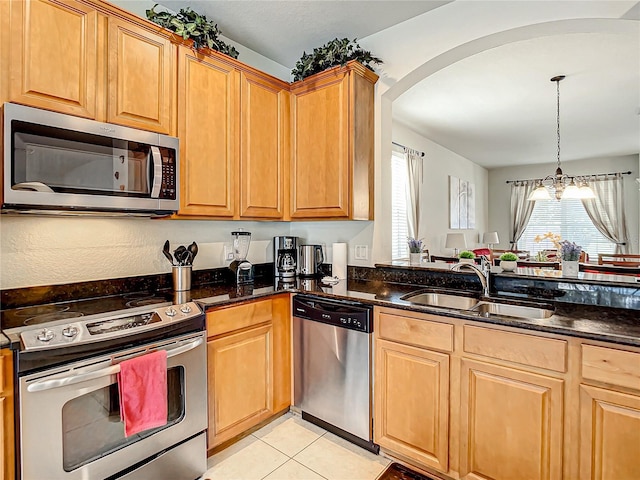 kitchen featuring light tile patterned floors, dark stone countertops, appliances with stainless steel finishes, and a sink