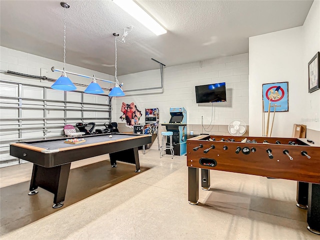 game room with a garage, concrete block wall, pool table, and a textured ceiling