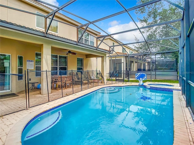 view of pool with glass enclosure, a pool with connected hot tub, a patio area, and a ceiling fan