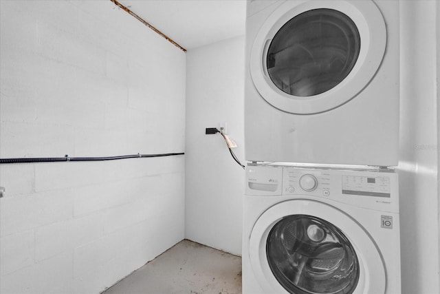 washroom featuring laundry area, stacked washing maching and dryer, and concrete block wall