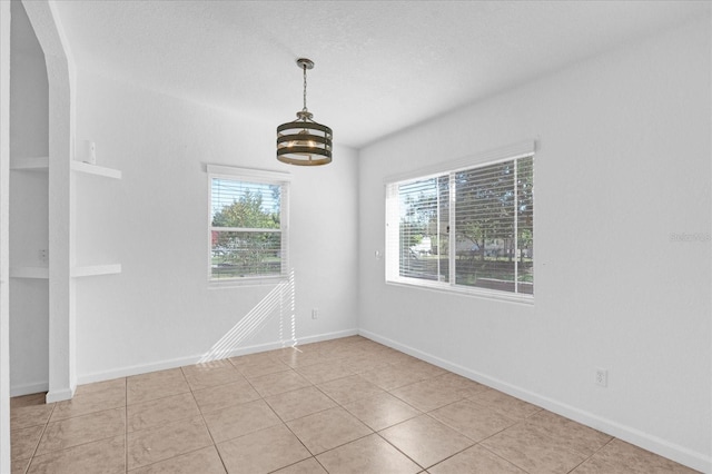 spare room featuring light tile patterned flooring, arched walkways, a textured ceiling, and baseboards