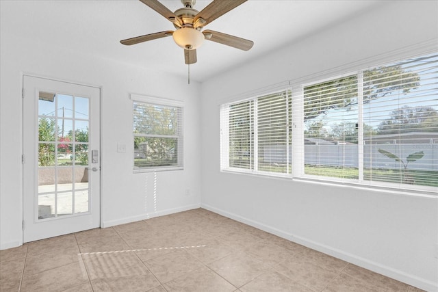 empty room featuring light tile patterned floors, a ceiling fan, and baseboards