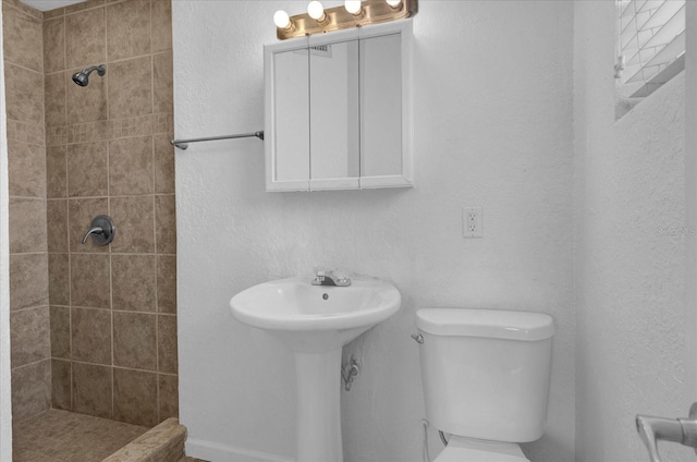 bathroom featuring a textured wall, toilet, a sink, and a tile shower