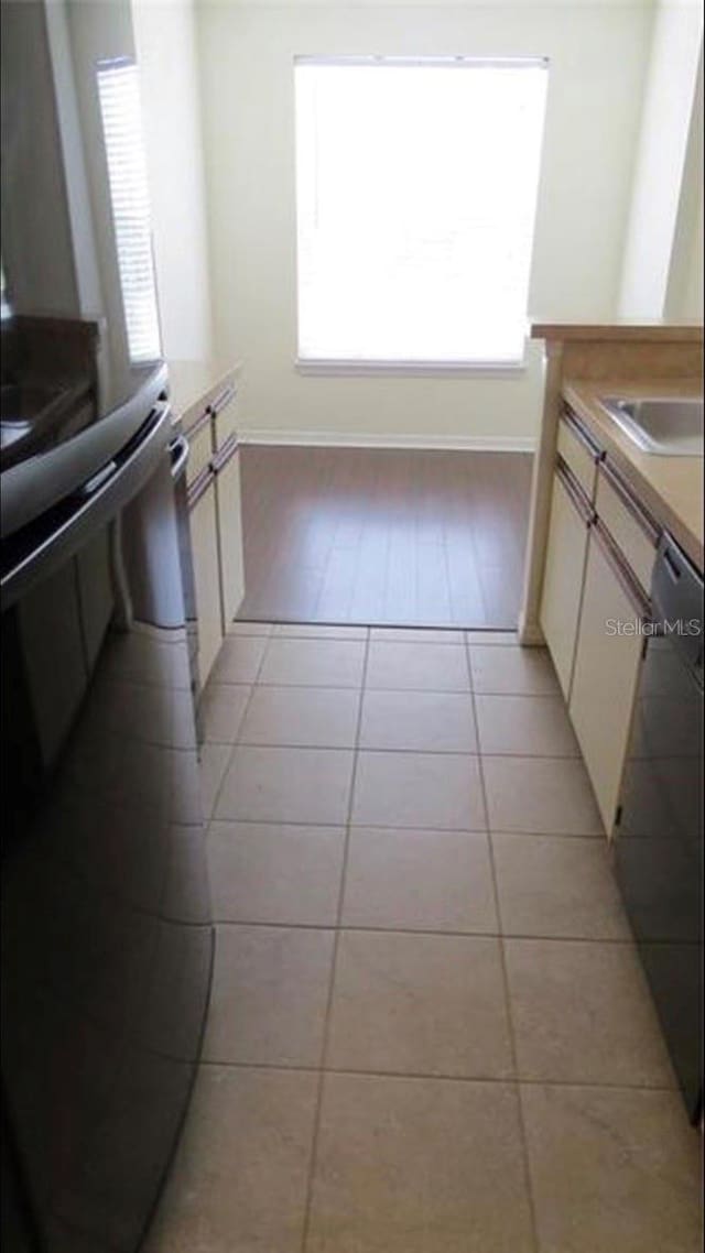 kitchen featuring black dishwasher, light tile patterned flooring, a sink, range, and baseboards
