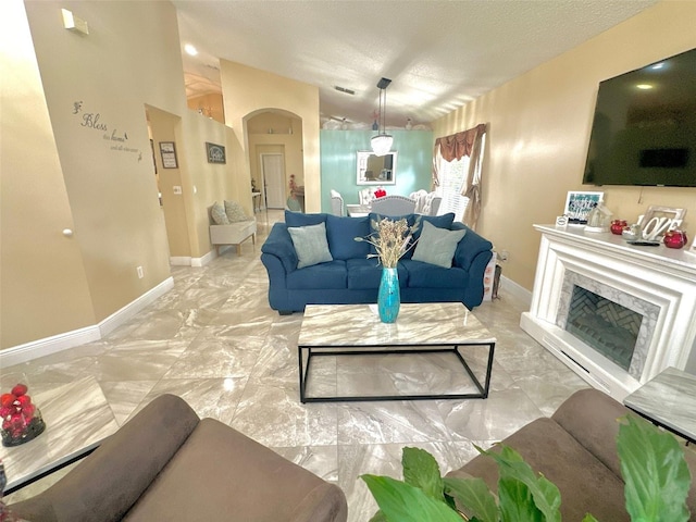 living area featuring arched walkways, marble finish floor, a premium fireplace, a textured ceiling, and baseboards