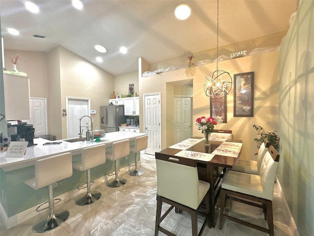 kitchen with a breakfast bar, a sink, white cabinetry, vaulted ceiling, and stainless steel fridge