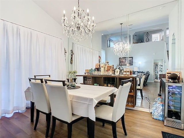 dining area with wine cooler, a dry bar, a towering ceiling, wood finished floors, and a notable chandelier