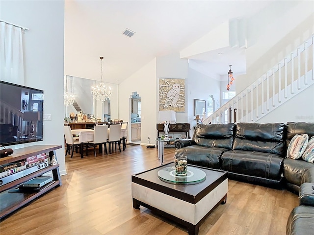 living room with light wood finished floors, visible vents, stairs, a notable chandelier, and high vaulted ceiling