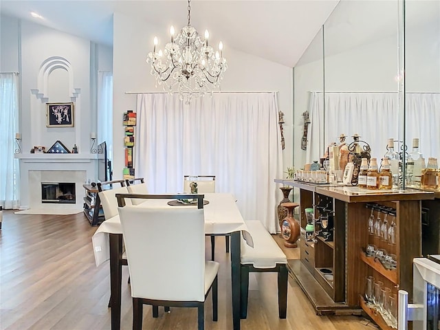 dining space featuring a chandelier, wood finished floors, a glass covered fireplace, and vaulted ceiling