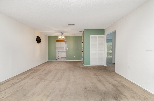 spare room with a textured ceiling, a notable chandelier, light colored carpet, visible vents, and baseboards