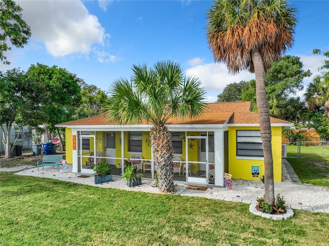 rear view of house with stucco siding, fence, a yard, and a sunroom