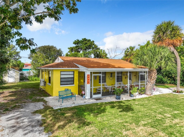 bungalow-style house with a shingled roof, a front yard, a sunroom, and stucco siding