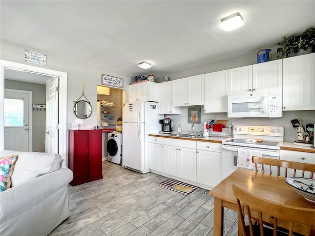 kitchen featuring a sink, white cabinetry, white appliances, light wood-style floors, and washer / dryer