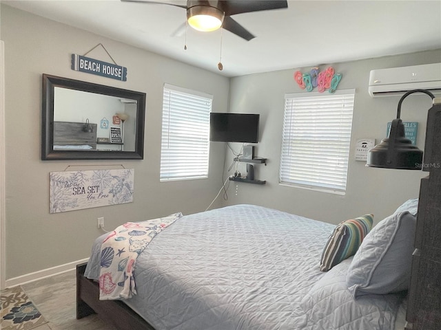 bedroom featuring wood finished floors, baseboards, ceiling fan, and a wall mounted AC